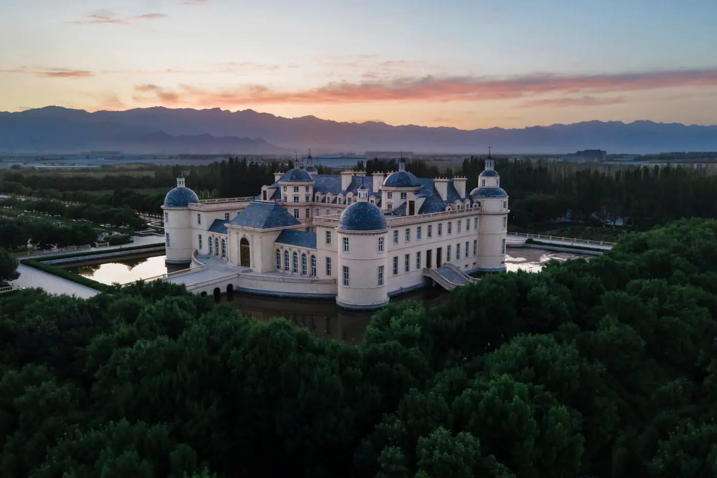 Chateau Changyu Moser XV from the air at sunrise, surrounded by its moat and forest, the Helan Mountains behind
