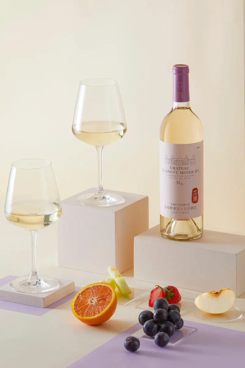 A bottle of White Cabernet with two filled glasses, grapefruit and grapes